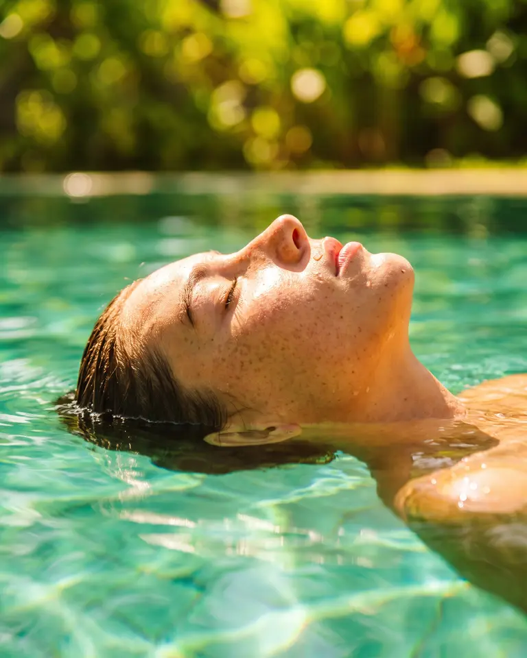 A woman floating on her back in deep green water, only her face above the surface.
