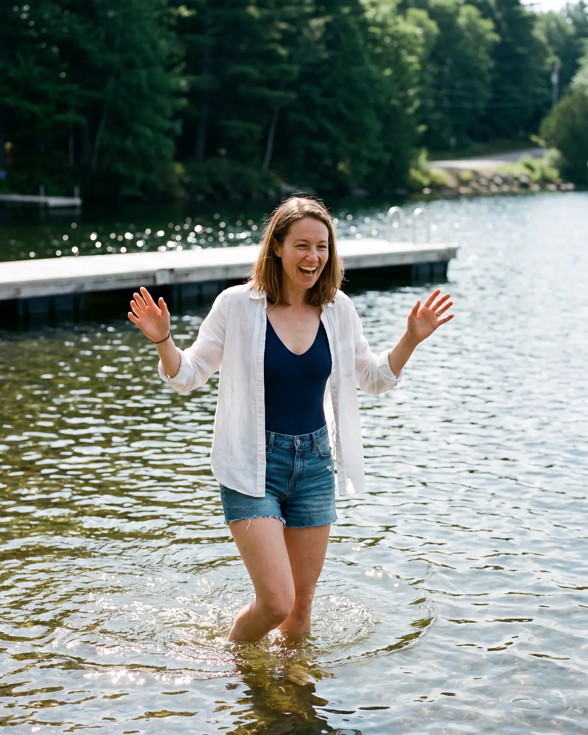 Una mujer entrando a un lago frío en verano, riéndose con los brazos en alto.